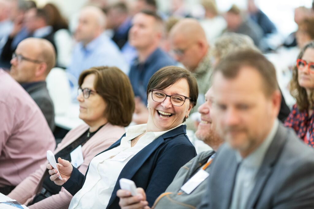 Group of diverse adults smiling and engaging during an indoor business meeting, showcasing teamwork.